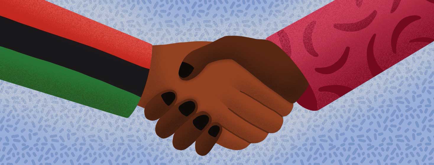 A person wearing an African American flag shirt shakes hands with a person wearing a shirt with sickle cells on it.
